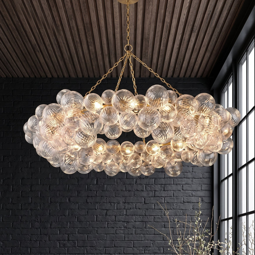 Lustre couronne à bulles de verre et structure en laiton doré, suspendu au-dessus d'un salon aux murs de briques noires et au plafond en lattes de bois.